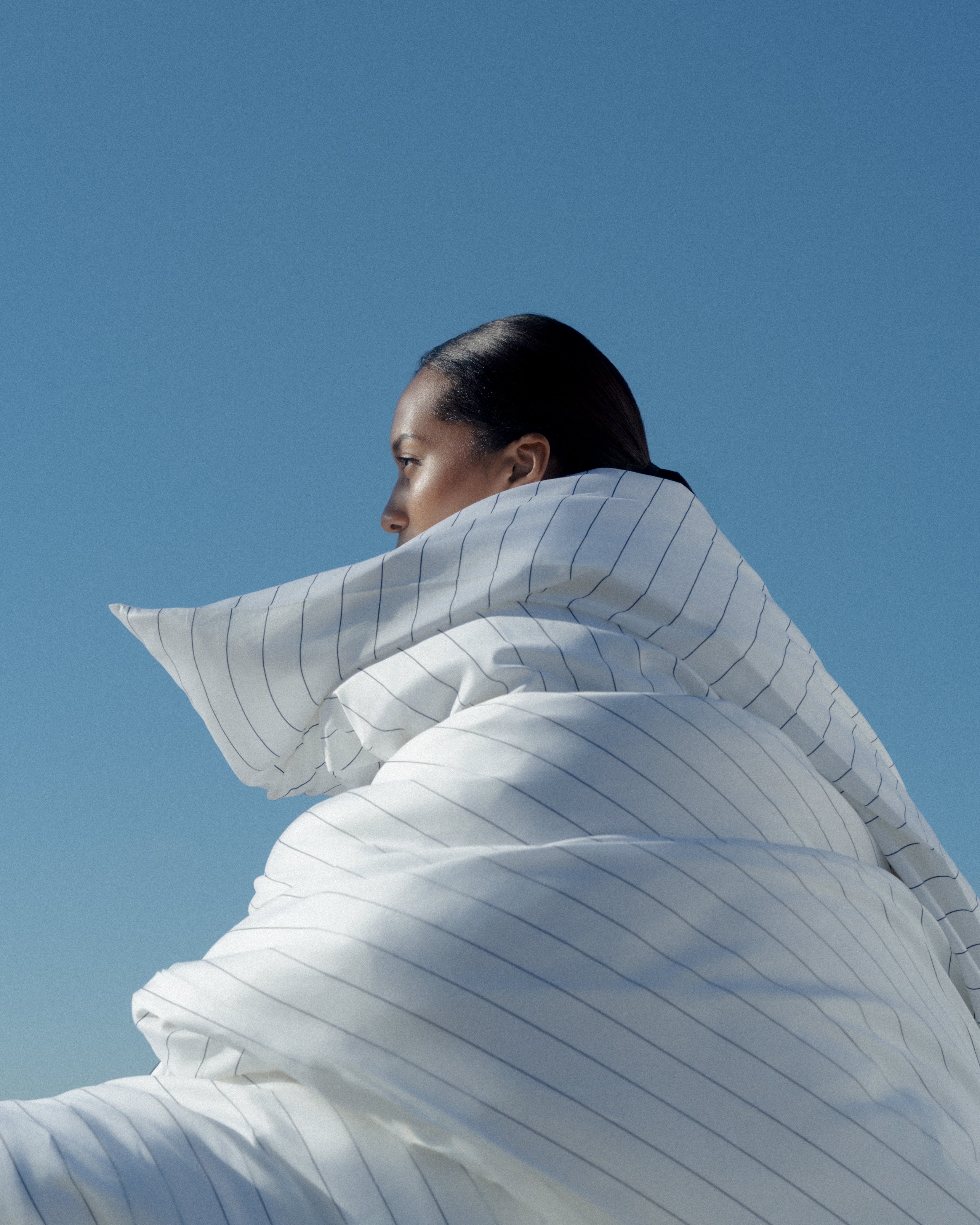 Person wrapped in a large white duvet against a clear blue sky