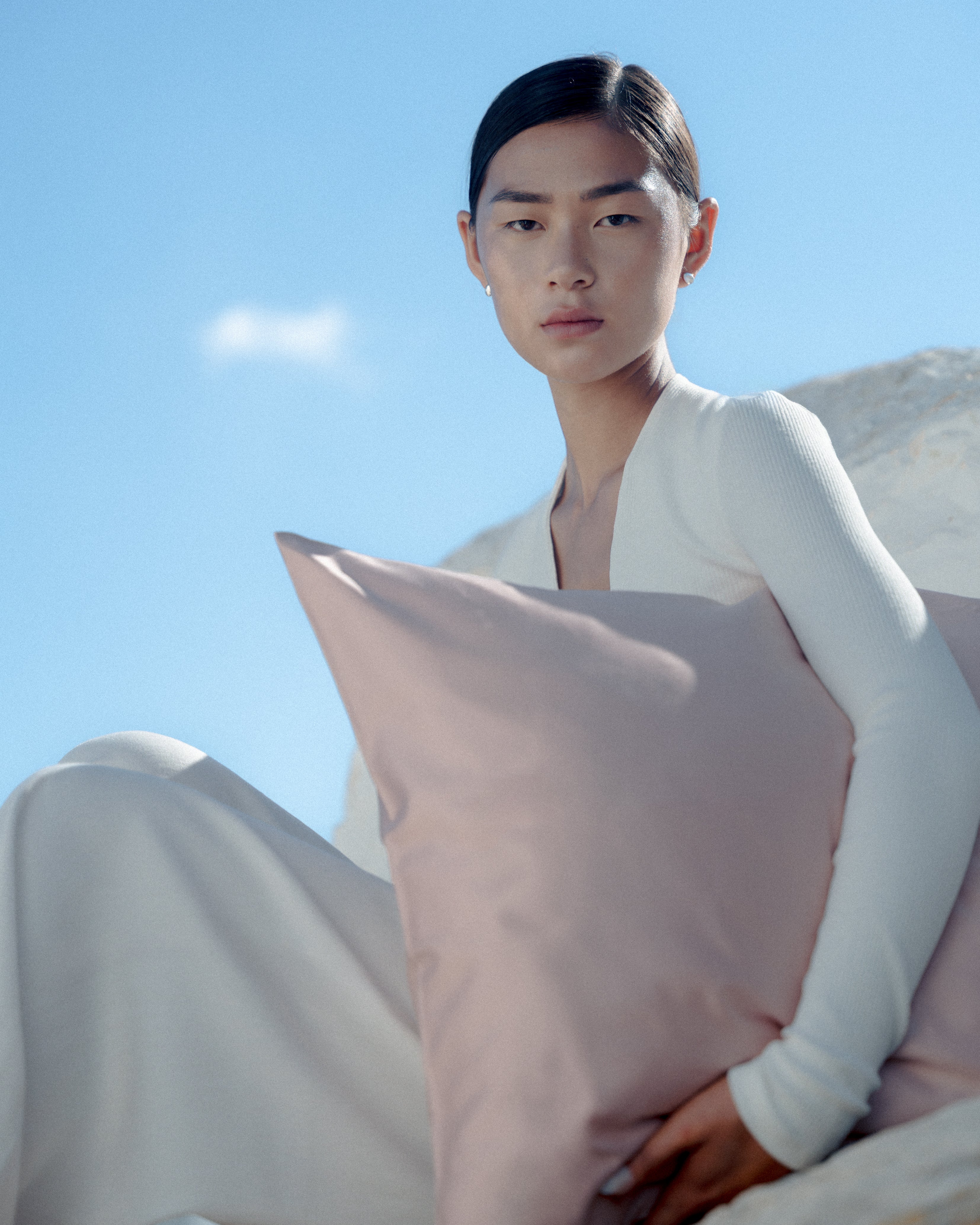 Person holding a pink pillow against a clear blue sky